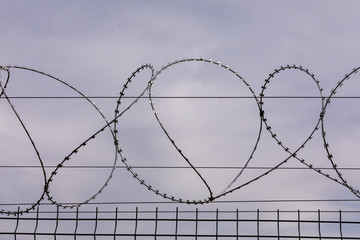 Barbed wire against the cloudy sky. Barbed wire fencing from the prison fence. The concept of captivity, slavery, prisoners, convicted. Prison, checkpoint, security territory, border, military base.