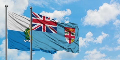 San Marino and Fiji flag waving in the wind against white cloudy blue sky together. Diplomacy...