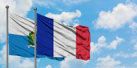 San Marino and France flag waving in the wind against white cloudy blue sky together. Diplomacy...