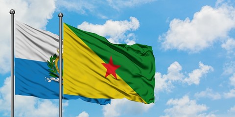 San Marino and French Guiana flag waving in the wind against white cloudy blue sky together. Diplomacy concept, international relations.