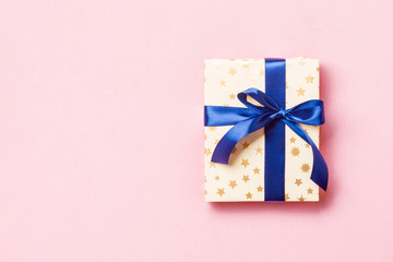 wrapped Christmas or other holiday handmade present in paper with blue ribbon on pink background....