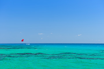 Water of the tropical turquoise sea with a boat and a red parachute. Parasailing.