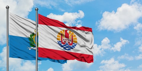 San Marino and French Polynesia flag waving in the wind against white cloudy blue sky together. Diplomacy concept, international relations.