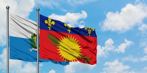 San Marino and Guadeloupe flag waving in the wind against white cloudy blue sky together. Diplomacy concept, international relations.
