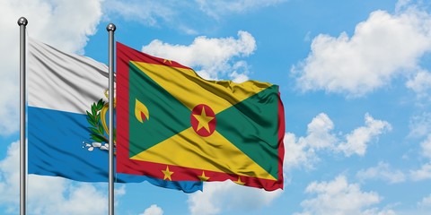 San Marino and Grenada flag waving in the wind against white cloudy blue sky together. Diplomacy concept, international relations.