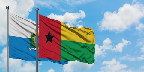 San Marino and Guinea Bissau flag waving in the wind against white cloudy blue sky together. Diplomacy concept, international relations.