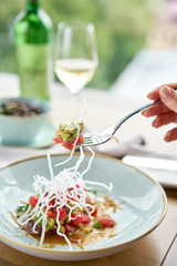 Closeup fork with pieces of food. Woman eating tartar in the restaurant. Variety of dishes on the table. Italian cuisine