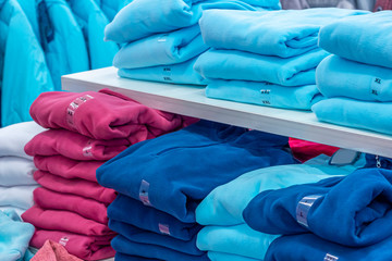 Warm clothing neatly folded on a shelf. A row of colorful jumpers, cardigans, sweatshirts,...