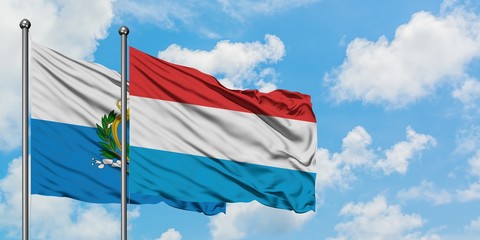 San Marino and Luxembourg flag waving in the wind against white cloudy blue sky together. Diplomacy concept, international relations.