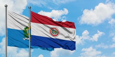 San Marino and Paraguay flag waving in the wind against white cloudy blue sky together. Diplomacy concept, international relations.