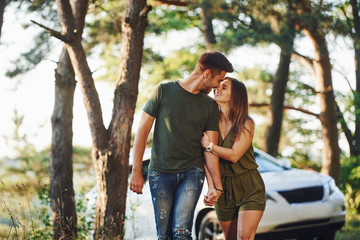 Having a walk. Car behind. Beautiful young couple have a good time in the forest at daytime