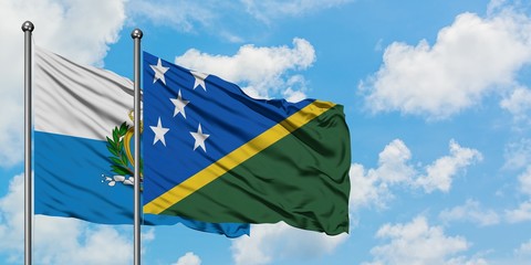 San Marino and Solomon Islands flag waving in the wind against white cloudy blue sky together. Diplomacy concept, international relations.