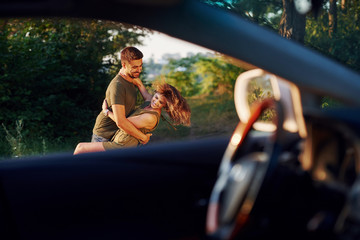 View through the car's window. Beautiful young couple have a good time in the forest at daytime