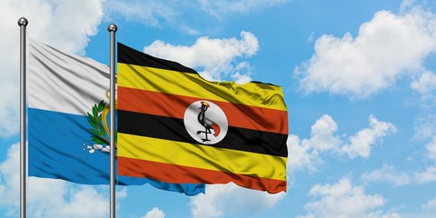San Marino and Uganda flag waving in the wind against white cloudy blue sky together. Diplomacy...