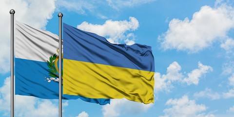 San Marino and Ukraine flag waving in the wind against white cloudy blue sky together. Diplomacy concept, international relations.