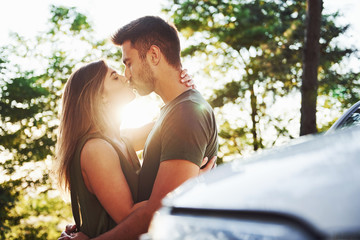 Fototapeta premium Front part of white car. Beautiful young couple have a good time in the forest at daytime