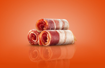 Fototapeta na wymiar Palatable slices of a rolled bacon on an orange background with copy space for text or images, mirror surface. Advertising concept. Close-up shot.