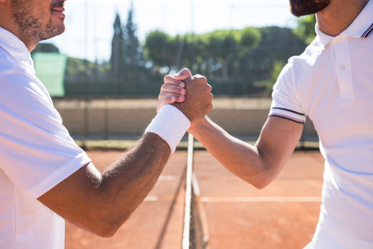 Side view of two tennis players with rackets shaking hands and smiling before tennis match