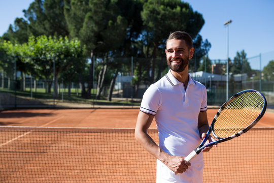 Attractive bearded man in tennis wear holding racket and looking away