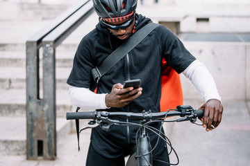 Stylish young man with bicycle, smartphone and messenger bag in the city