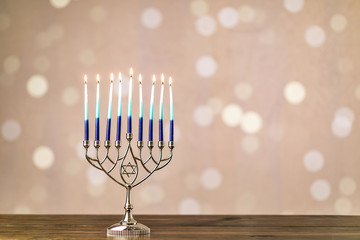 A silver menorah for the Jewish holiday Hanukkah with burning glowing eight candles on fire lit up on a beige background with copy space