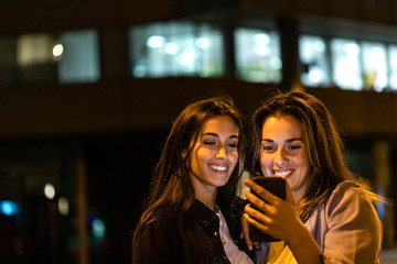 Two friends using the smartphone at night, with city lights in the background
