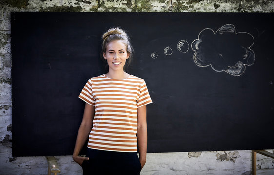Smiling young woman standing in front of a blackboard next to a thought bubble