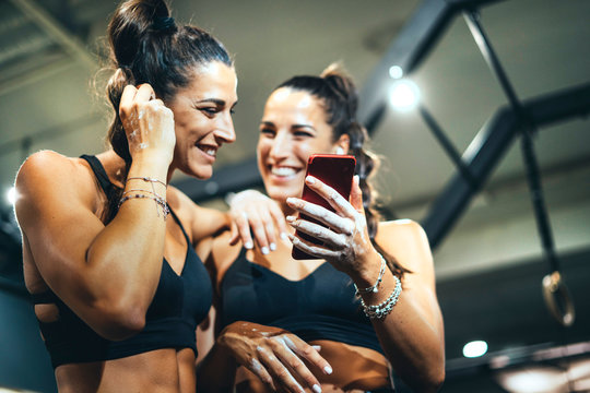 Smiling female, twins in good shape using smartphone in a gym