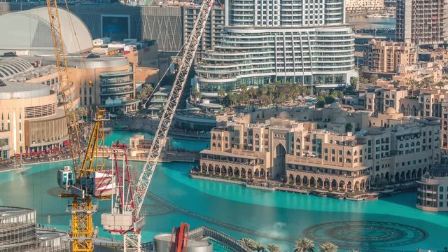 Unique view of Dubai Fountains pool at evening timelapse. Tourist attraction. Aerial view with Old Town Island from above and cranes on construction site