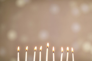 A silver menorah for the Jewish holiday Hanukkah with burning glowing eight candles on fire lit up on a beige background with copy space