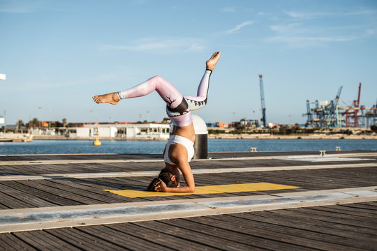 Asian woman practicing yoga on a pier at harbor, headstand with split