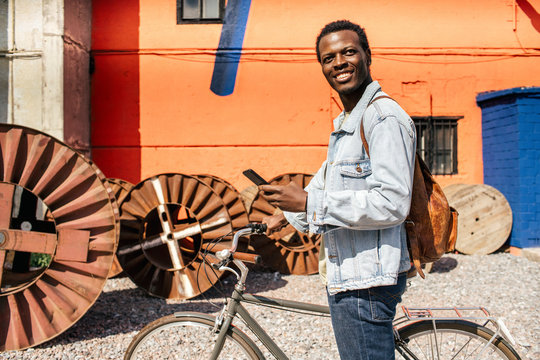Relaxed young man commuting in the city with hos bicycle, using smartphone