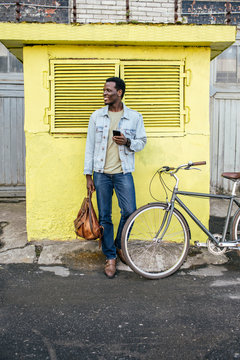 Young man with smartphone, waiting in front of yellow junction box