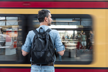 Rear view of man with backpack at the station platform while train coming in, Berlin, Germany