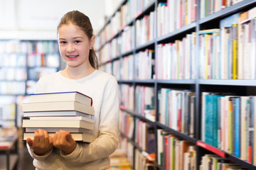 Cheerful preteen girl holding stack of books