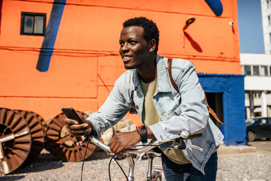 Relaxed young man commuting in the city with hos bicycle, using smartphone