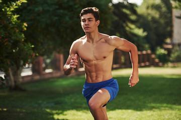 Going forward. Muscular shirtless man have fitness day and running in the park at daytime