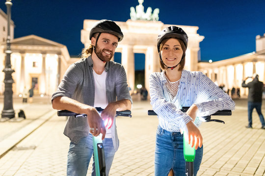 Young couple with electric scooters at Brandenburg Gate at night, Berlin, Germany