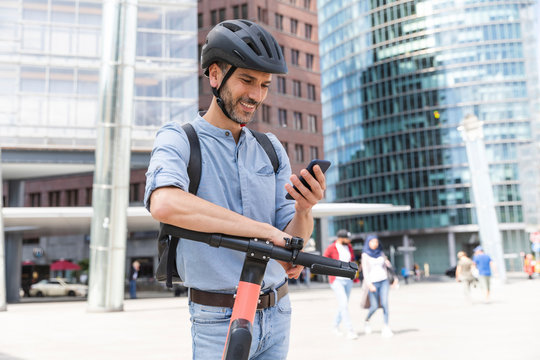 Smiling businessman looking at the smartphone commuting on electric scooter in the city, Berlin, Germany