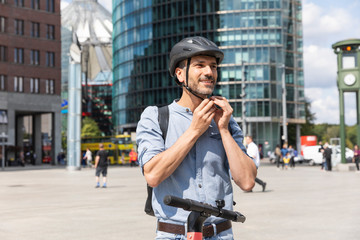 Man fastening the helmet before riding on electric scooter, Berlin, Germany