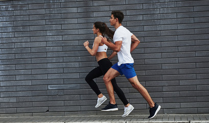 Healthy lifestyle. Man and woman have fitness day and running in the city at daytime near brick wall