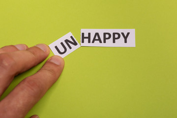 man hand holding card with text unhappy, cutting word 'un' so it written 'happy'. Copy space. Lime background. Studio shoot