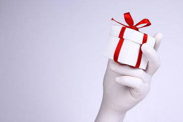 Gift box in a hand. Hand with white glove holding white gift box with red ribbon. Christmas and New Year holidays concept on white background.