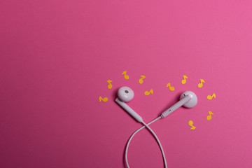 white earphones and yellow paper notes on pink background. view from above.