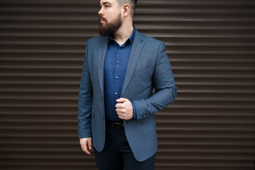Stylish handsome brunette man with beard, wearing suit jacket and blue shirt, outdoors on the city...