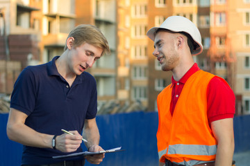 Two engineer builders with blueprint plan at construction site