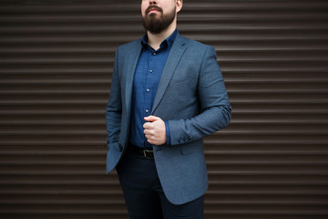 Stylish handsome brunette man with beard, wearing suit jacket and blue shirt, outdoors on the city...