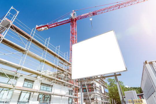 Blank white billboard in front of construction site with scaffolding and crane