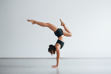 Doing hand stand. Young sporty woman in black clothes with slim body type in the healthy center...