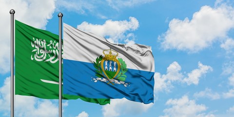 Saudi Arabia and San Marino flag waving in the wind against white cloudy blue sky together. Diplomacy concept, international relations.
